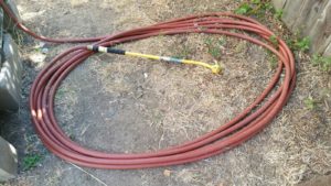 Garden hose with handheld wand coiled up near tote.